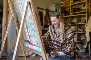 Crafty woman weaving at a loom at her workshop
