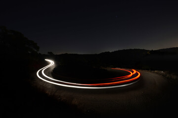 A photo of a car's light trails on a curvy turn during the night with a dark background 