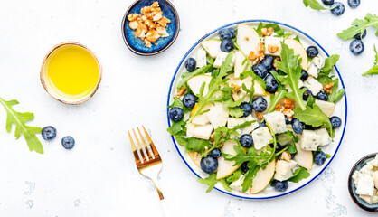 Gourmet summer salad with sweet pears, blueberries, blue cheese, arugula and walnuts. White kitchen table background, top view