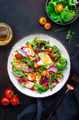 Gourmet salad with grilled salmon with tomatoes, cucumber, arugula, radicchio, red onion and lettuce with lemon oil dressing. Healthy lunch. Brown stone table background, top view