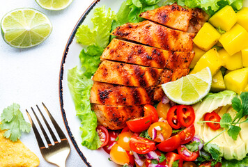 Yummy salad with grilled chicken fillet with mango, spicy salsa, tomatoes, cilantro, red onion and lettuce in tex-mex style, white table background, top view