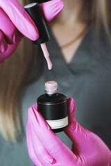 A manicurist wearing gloves holds gel polish on a white background