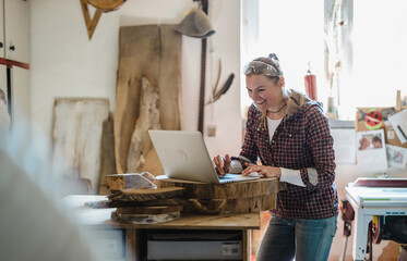 Female carpenter using laptop in a carpentry workshop
