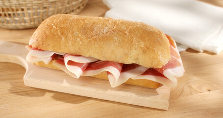 Ciabatta Sandwich with Prosciutto on a wooden background. Bread basket, tomatoes and bacon or jamon sandwich. Italian food. Rustic still life. Sunny day. Close up shot.