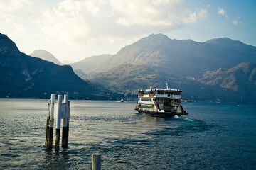 Lake Como from the shore of the town of Bellagio. View of the Alps mountains, buildings and a passenger ferry. Sunset