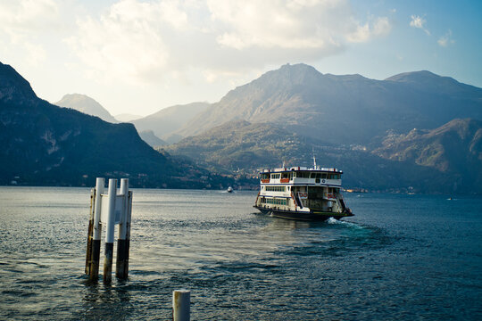 Lake Como from the shore of the town of Bellagio. View of the Alps mountains, buildings and a passenger ferry. Sunset