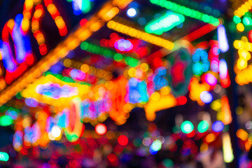 Blurred lights of a carousel with colorful led illumination on a fun fair in Menden Germany. Unfocused glowing yellow, green, blue, red lights at night. Fairground attraction background.