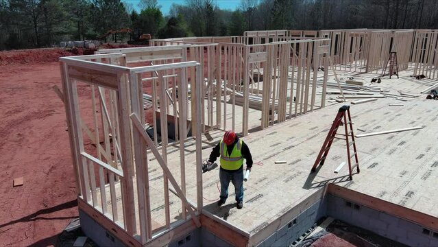 Contractor is hammering nail as he builds new wooden house by framing