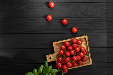Green fresh vegetables, small tomatoes and basilica on black wooden background. Flat lay