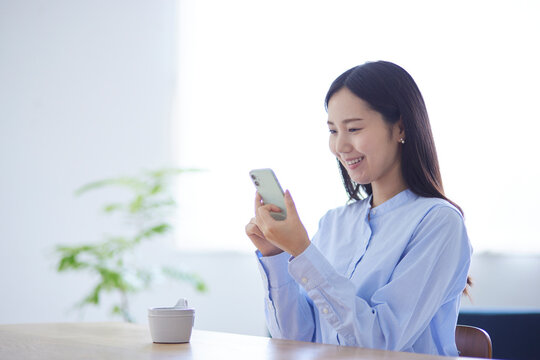 リビングでリラックスしながらスマートフォンを操作する20代日本人女性の夏のイメージ
