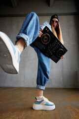 A young pretty long-haired DJ girl in a blue sweater, jeans and a black baseball cap poses with a...