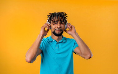 Enjoying african bearded man listening music, posing with headphones on yellow