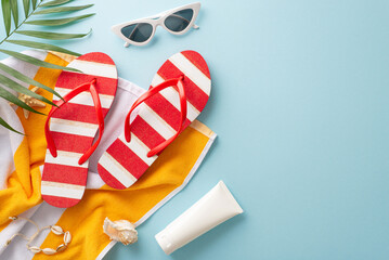 Tropical getaway concept. Top view of vacation accessories: flip-flops, sunscreen, towel, seashell bracelet, palm leaves, sunglasses. Empty space for text or ad on pastel blue background