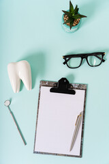 Dental and oral care concept. Dentist visit plan. Healthy tooth model, dentist mirror, glasses and notepad on blue background. Top view, copy space, mock up