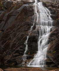 Fototapeta na wymiar Silky waterfall flowing over vertical rock formation, long exposure, space for text