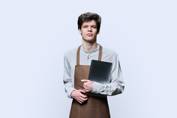 Young male in an apron with laptop, on blue background