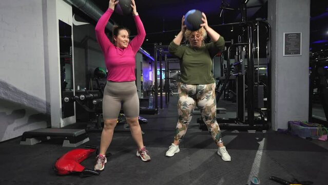 Two plus-size women workout and exercise with medicine ball at the gym. They're determined to achieve their goals and inspire others along the way.	
