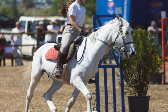 A girl in white uniform riding white horse at the ranch