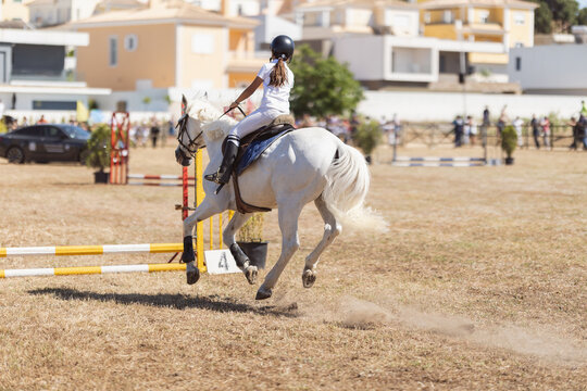 Equestrian sport - a girl in uniform riding white horse at the ranch - jumping over the obsticles