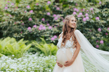 Fototapeta na wymiar A beautiful pregnant woman wearing a luxurious dress is standing in a blooming rhododendron garden
