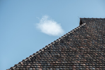 Detail Walmdach mit historischen Dachziegeln vor blauem Himmel mit weisser Wolke