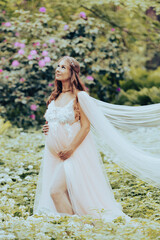 Fototapeta na wymiar A beautiful pregnant woman wearing a luxurious dress is standing in a blooming rhododendron garden