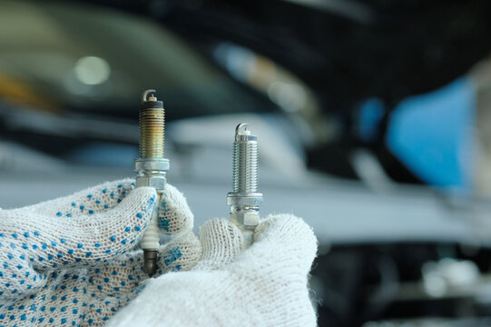 Spark plugs for an internal combustion engine. Close-up. An auto mechanic holds two spark plugs in his hands, one used, the other new. An auto mechanic demonstrates their external difference.