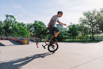 A professional middle-aged tattooed bmx bike rider is performing freestyle tricks in a skate park...