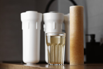 Water filter cartridge used and a glass of rusty water brown coloring on wooden table at kitchen...