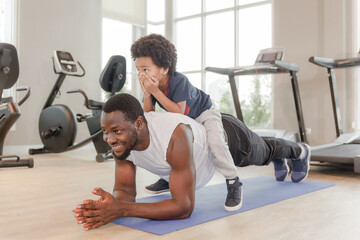 Cute boy in sportswear with smiling african american black father doing yoga on yoga mat in morning with