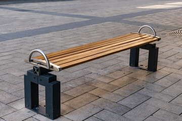 Stylish wooden bench with a metal frame on the pavement covered with stone tiles.