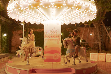 Male traveler take a photo his girl friend in carousel at theme park in holiday, contain word...