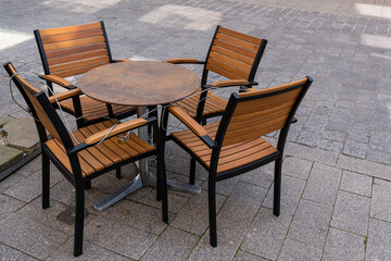 Wooden chairs and a table of a street cafe closed with a metal cable and a padlock
