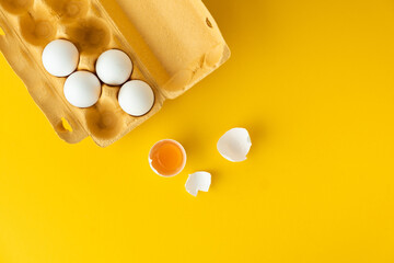 Flat lay of white eggs in the carton brown box on the yellow background. Top view of broken egg...