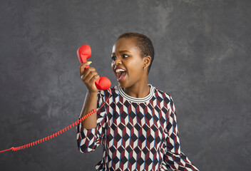 Angry african american woman irritated and angrily shouting into the phone arguing with the...