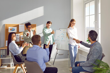 Businesswoman shaking hands with businessman while their colleagues applauding them. Smiling male and female employees holding hands during office meeting. Team appreciating performance of colleagues