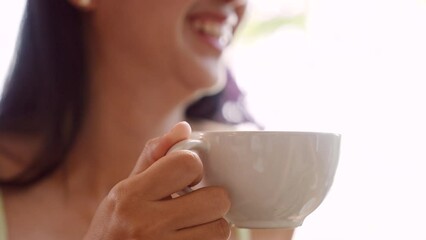 Close-up shot of white glass filled with latte coffee Being lifted in the hands of a young Asian woman lifting up to drink coffee In the bakery Selling coffee drinks. woman smiling and talking