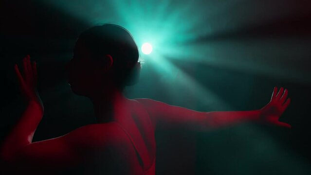 Graceful plastic performer dancing on stage with dramatic colorful light. Female ballet dancer performing elements of modern choreography. Beautiful young ballerina in contemporary dance show