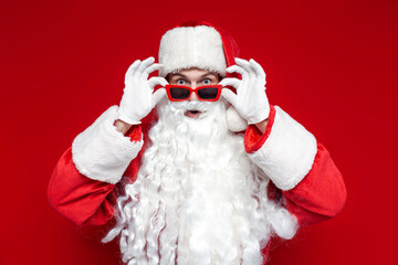 shocked santa claus in red glasses looks at the camera in surprise and is amazed on colored background