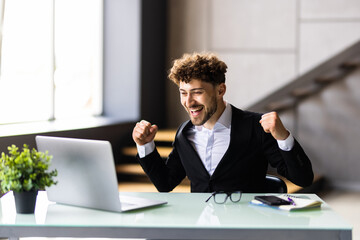 Happy businessman achiving his goal and showing fists at office