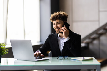 Bearded man at the wooden desk talking on the phone in office