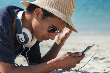 young man with worried or serious gesture with headphones and mobile phone on the beach