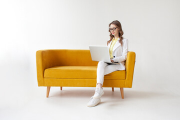 young businesswoman in suit sits on comfortable soft sofa and uses laptop, girl in formal wear is...