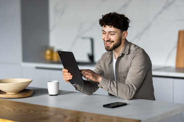 Portrait of a young man in the kitchen with a tablet at home