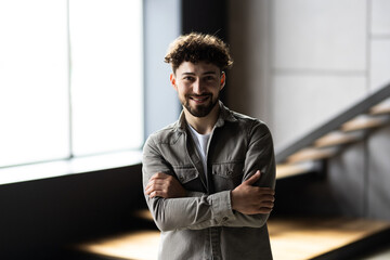 Happy confident businessman in casual standing with arms crossed at work table in home office