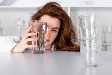 A girl is looking through a glass of water, visually distorting her face. emonstrating product...