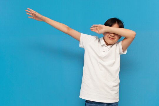 teenager boy in white t-shirt makes dub gesture and covers his face with his hands on blue background