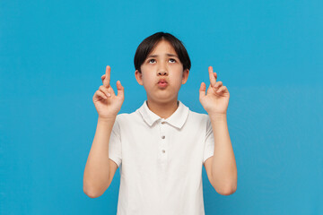 asian boy hope for good luck with fingers crossed and believe on blue isolated background, korean child