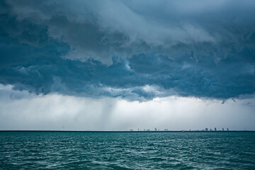 View of tropical ocean storm with menacing clouds and rain showering below, Light in the dark and dramatic storm clouds background