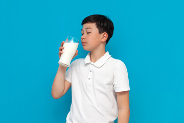 little asian boy in white t-shirt holds glass of milk on blue background, korean child shows and recommends